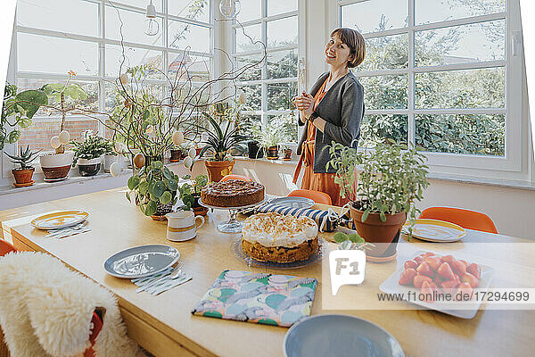 Woman smiling while standing by dining table at home