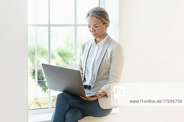 Geschäftsfrau mit Laptop auf der Fensterbank sitzend