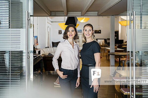 Lächelnde weibliche Fachkräfte stehen zusammen an der Tür in einem Büro