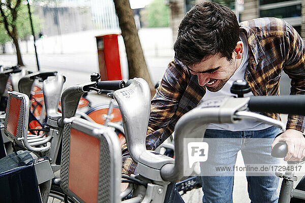Lächelnder junger Mann beim Aufschließen des Fahrrads am Bahnhof