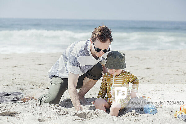 Father and son playing with sand at beach during sunny day