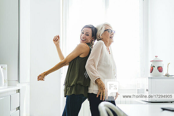 Lächelnde ältere Frau tanzt mit Enkelin in der Küche zu Hause