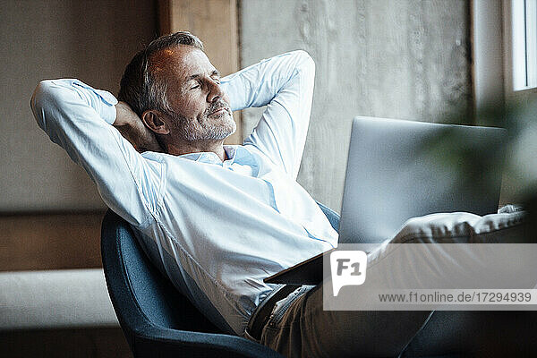 Älterer männlicher Unternehmer sitzt mit Laptop auf einem Stuhl