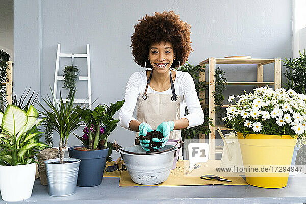Lächelnde Blumenhändlerin  die Erde in einen Blumentopf in einem Pflanzengeschäft gibt