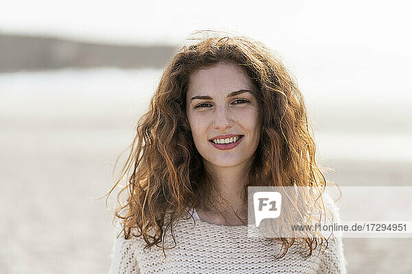 Schöne rothaarige Frau lächelnd am Strand