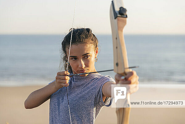 Junge Frau übt Bogenschießen am Strand