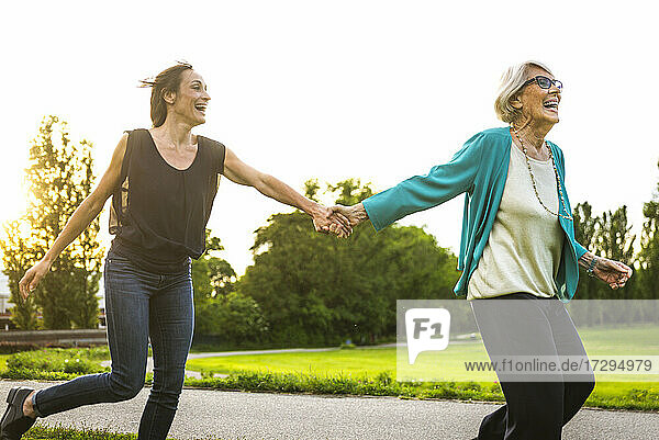 Verspielte Großmutter hält die Hand ihrer Enkelin beim Laufen im Park