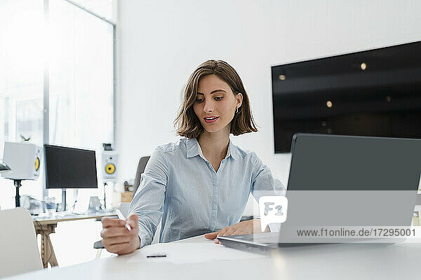 Young female professional sitting with laptop while working in office