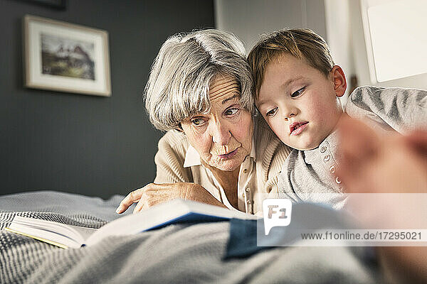 Großmutter  die ihrem Enkel im heimischen Schlafzimmer ein Buch vorliest