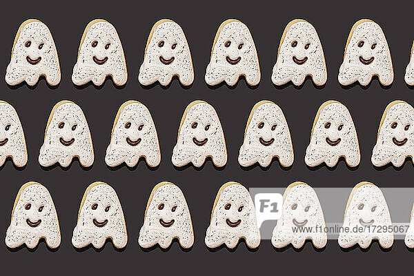Pattern of ghost-shaped chocolate cookies flat laid against black background