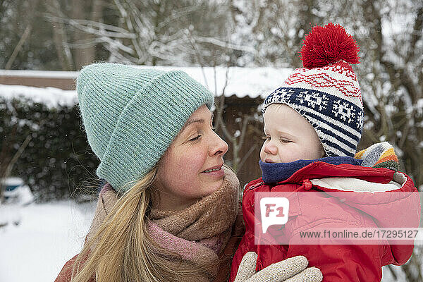 Lächelnde Mutter sieht ihren Sohn an  während sie im Hinterhof im Schnee steht