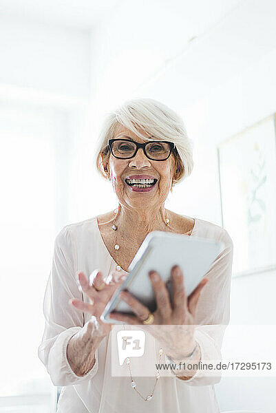 Glückliche ältere Frau mit Brille  die zu Hause ein digitales Tablet benutzt