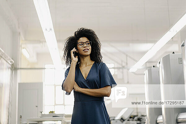 Female entrepreneur wearing eyeglasses talking on mobile phone in industry