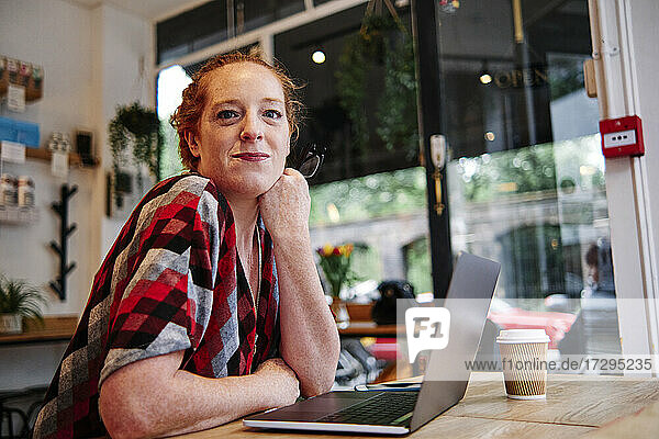 Mittlere erwachsene Frau lehnt sich in einem Café vor einem Laptop auf den Tisch