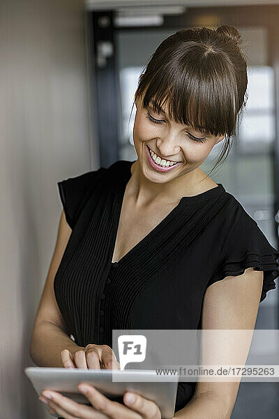 Junge lächelnde Geschäftsfrau mit Pony  die ein digitales Tablet im Büro benutzt