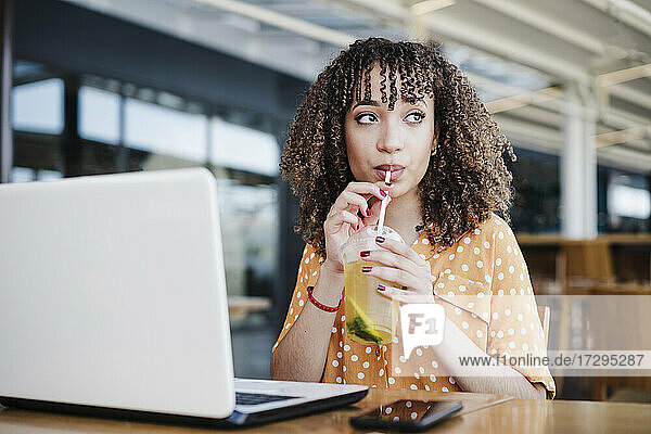 Junge Geschäftsfrau schaut weg  während sie in einem Café Eistee trinkt