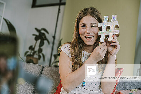 Lächelndes Teenager-Mädchen hält Hashtag-Symbol beim Filmen zu Hause