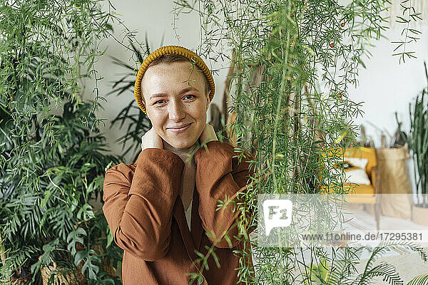 Lächelnde Geschäftsfrau mit Strickmütze bei Pflanzen im grünen Büro