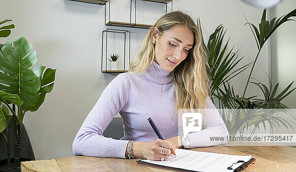 Blonde Geschäftsfrau  die am Schreibtisch sitzend im Büro Dokumente unterzeichnet