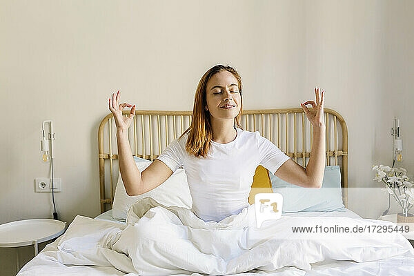 Rothaarige Frau meditiert auf dem Bett zu Hause