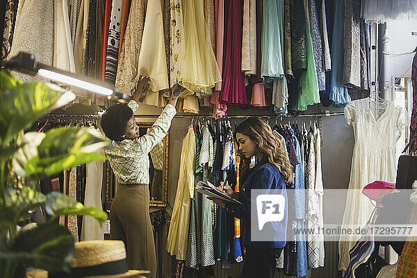 Weibliche Besitzerin macht sich Notizen  während ein Kollege die Kleidung in der Boutique ordnet