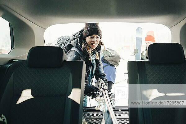 Mittlere erwachsene Frau lädt Skier in den Kofferraum eines Autos