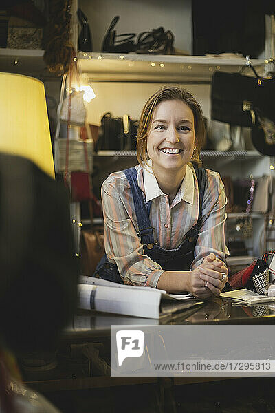 Porträt einer lächelnden Besitzerin  die sich in einem Geschäft auf einen Tisch lehnt