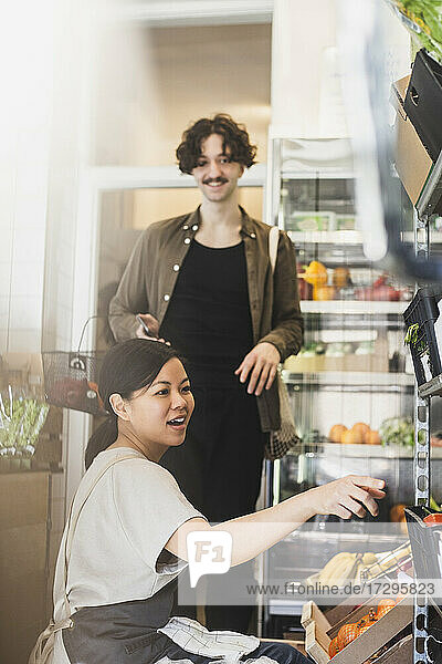 Lächelnder weiblicher Mitarbeiter  der auf ein Regal im Geschäft zeigt