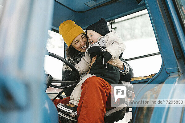 Fröhliche Mutter mit Tochter im Traktor sitzend im Winter