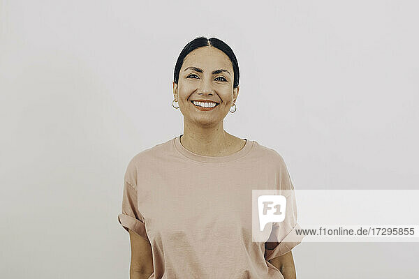 Porträt der lächelnden Frau trägt Pfirsich Farbe T-Shirt gegen weißen Hintergrund