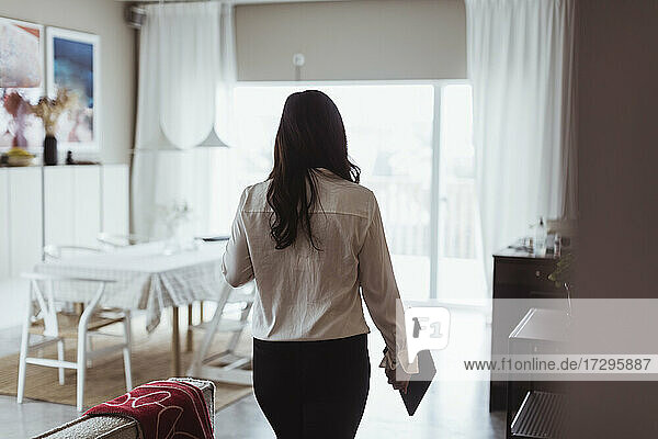 Rear view of businesswoman with digital tablet walking at home