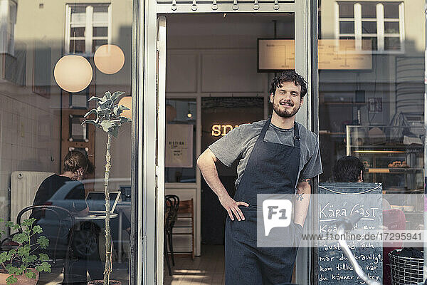 Portrait of smiling male entrepreneur leaning while standing at cafe entrance