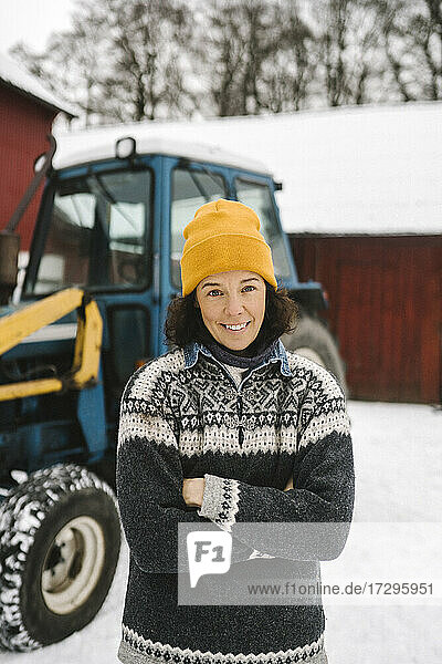 Porträt einer lächelnden Frau  die im Winter mit verschränkten Armen vor einem Traktor steht