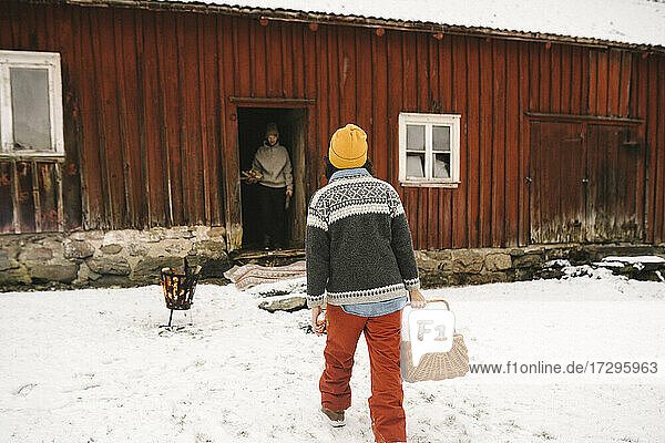 Ältere Frau trägt Korb beim Gehen in Richtung Hütte im Winter
