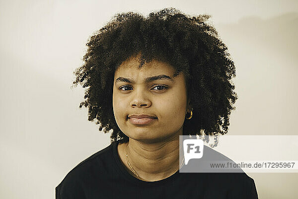 Portrait of confused young woman with curly hair against beige background