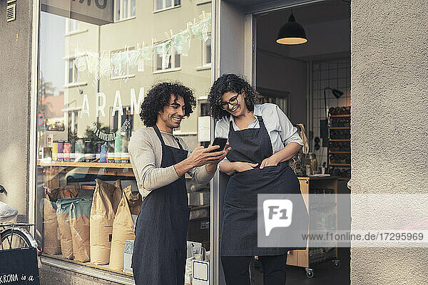 Fröhliche männliche und weibliche Besitzer teilen sich ein Smartphone an der Tür