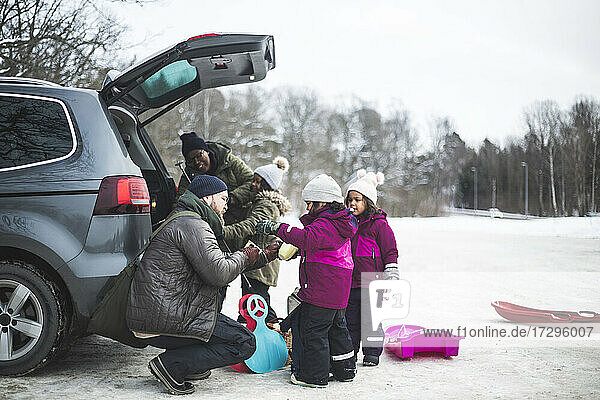 Mann hilft Tochter von Familie beim Entladen des Kofferraums im Winter