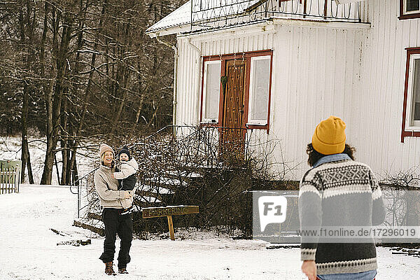 Ältere Frau zu Fuß in Richtung lächelnde Freundin trägt Tochter auf Schnee