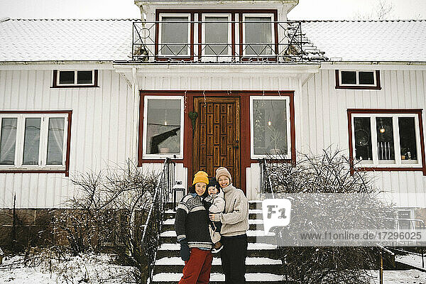 Porträt von glücklichen lesbischen Paar mit Tochter gegen Haus im Winter