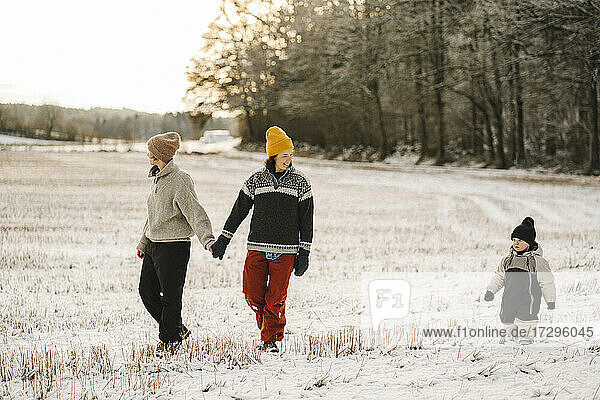 Gay couple holding hands while walking with daughter on snow during winter