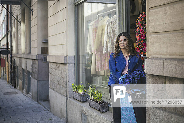Lächelnde Unternehmerin mit Kleidung an der Tür im Geschäft stehend