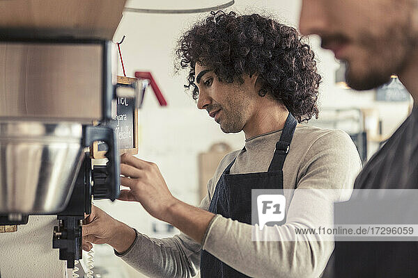 Männlicher Unternehmer macht Kaffee aus der Maschine  während er neben einem Mitarbeiter im Café steht