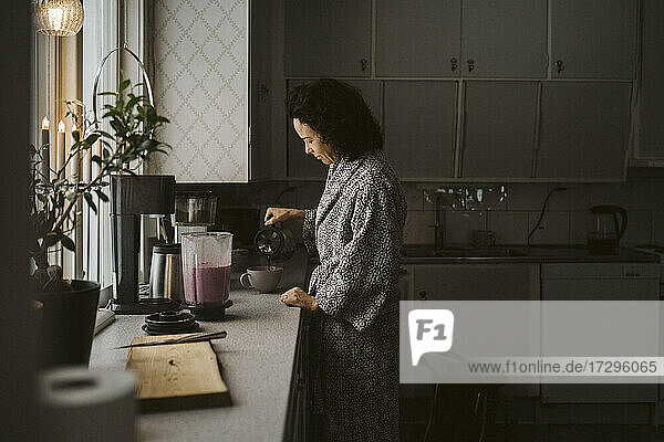 Reife Frau gießt Kaffee in Tasse am Küchentisch
