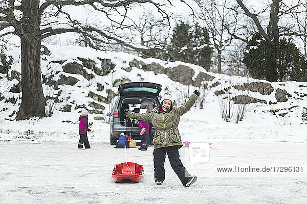 In voller Länge von glücklichen Mädchen stehen mit Schlitten auf Schnee gegen Familie