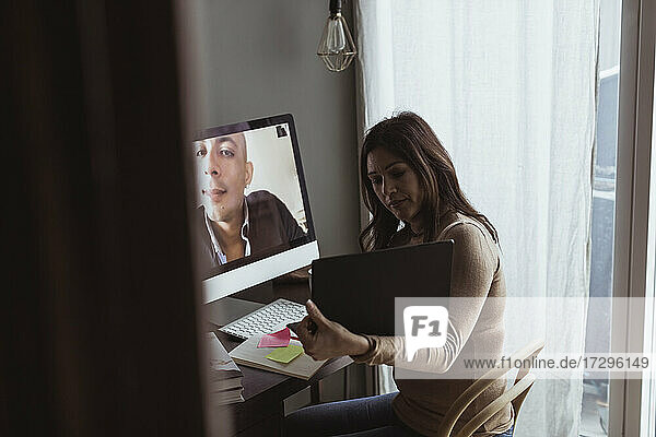 Geschäftsfrau zeigt Laptop an männlichen Profi auf Videoanruf im Home-Office