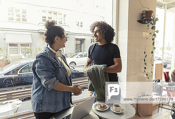 Glückliche männliche und weibliche Freunde reden  während sie im Café stehen