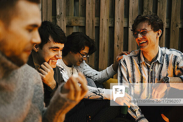 Happy young male friends talking while spending leisure time in balcony