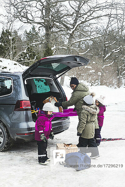 Mutter und Töchter beim Entladen von Gepäck aus dem Kofferraum eines Autos im Winter