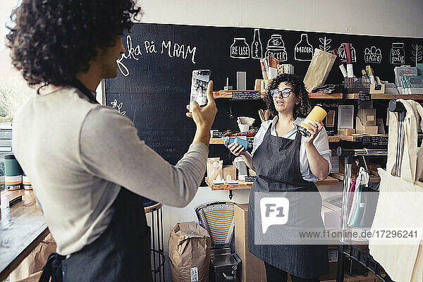 Male entrepreneur filming female co-owner advertising reusable bottles at organic shop
