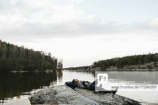 Weibliche Forscher entspannen auf Felsen am See gegen den Himmel im Urlaub